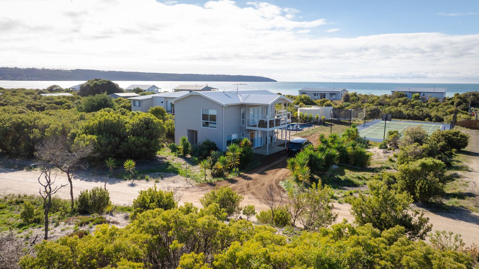 Aerial view of Island Beach House surrounded by coastal bush and the ocean beyond